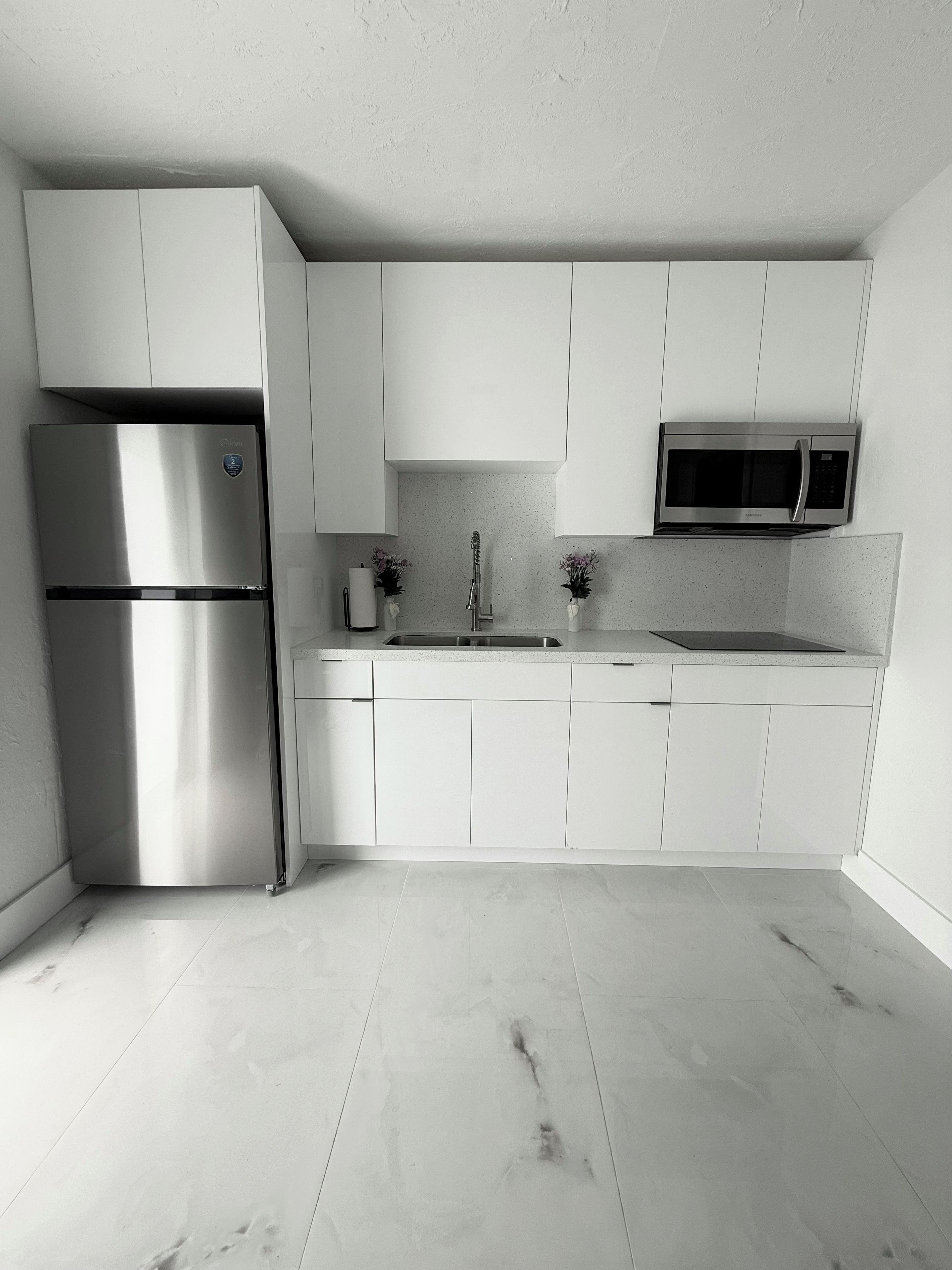 Cocina moderna con armarios blancos, refrigerador de acero inoxidable, microondas y pileta.