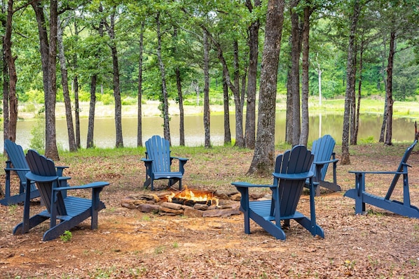 A campsite with four Adirondack chairs arranged around a campfire.