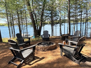 A lakeside seating area with Adirondack chairs and a fire pit.