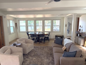 A spacious living room with a large window, a dining area with a table and chairs, and a cozy seating area with a sofa and armchairs.