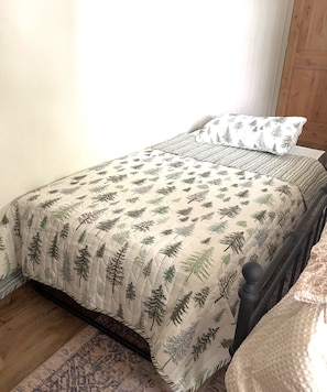A bed with a quilted bedspread featuring a forest leaf pattern, a matching pillow, and a wooden headboard.
