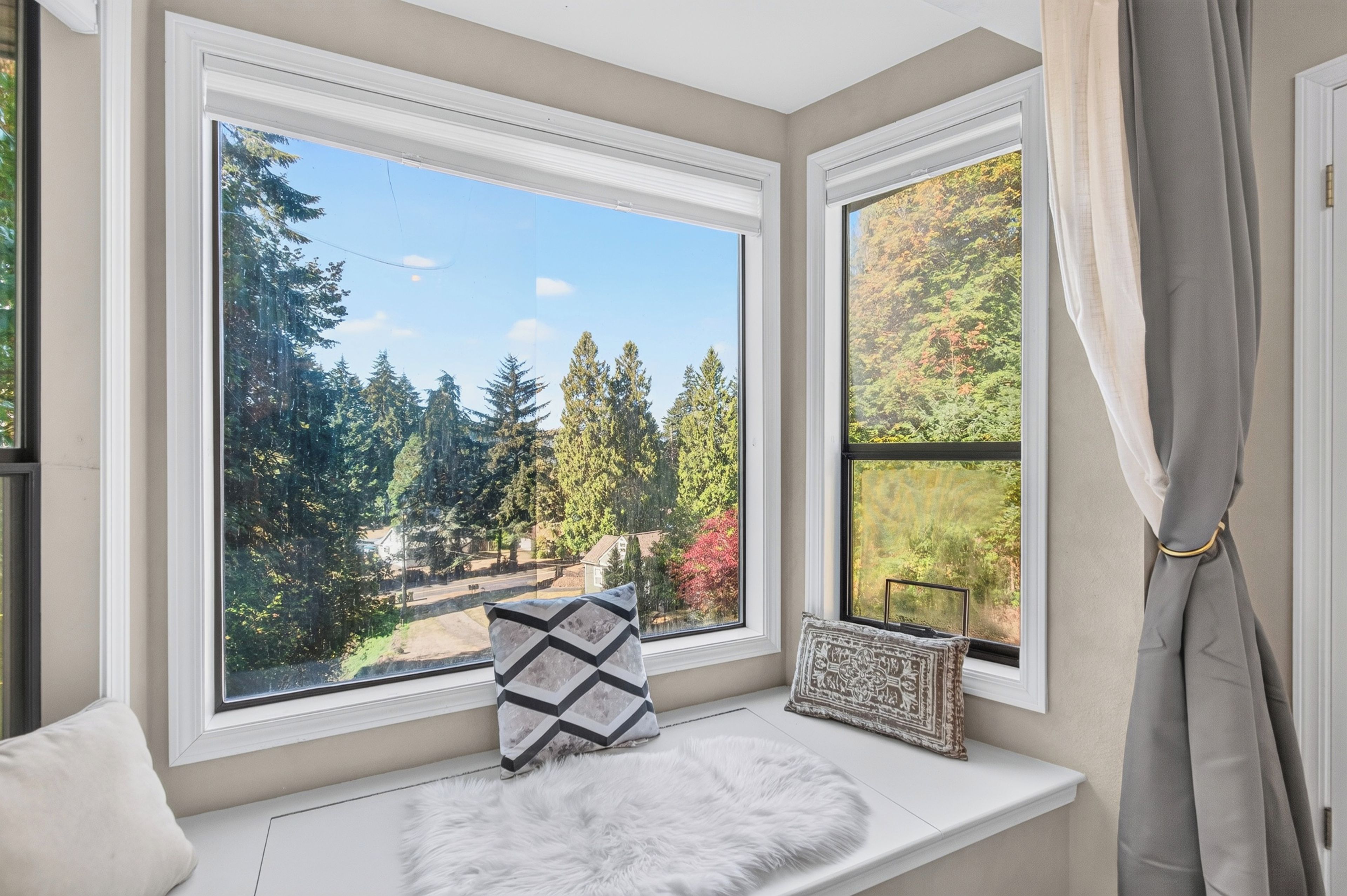 A room with a view of a forest through a bay window.