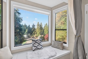 A room with a view of a forest through a bay window.
