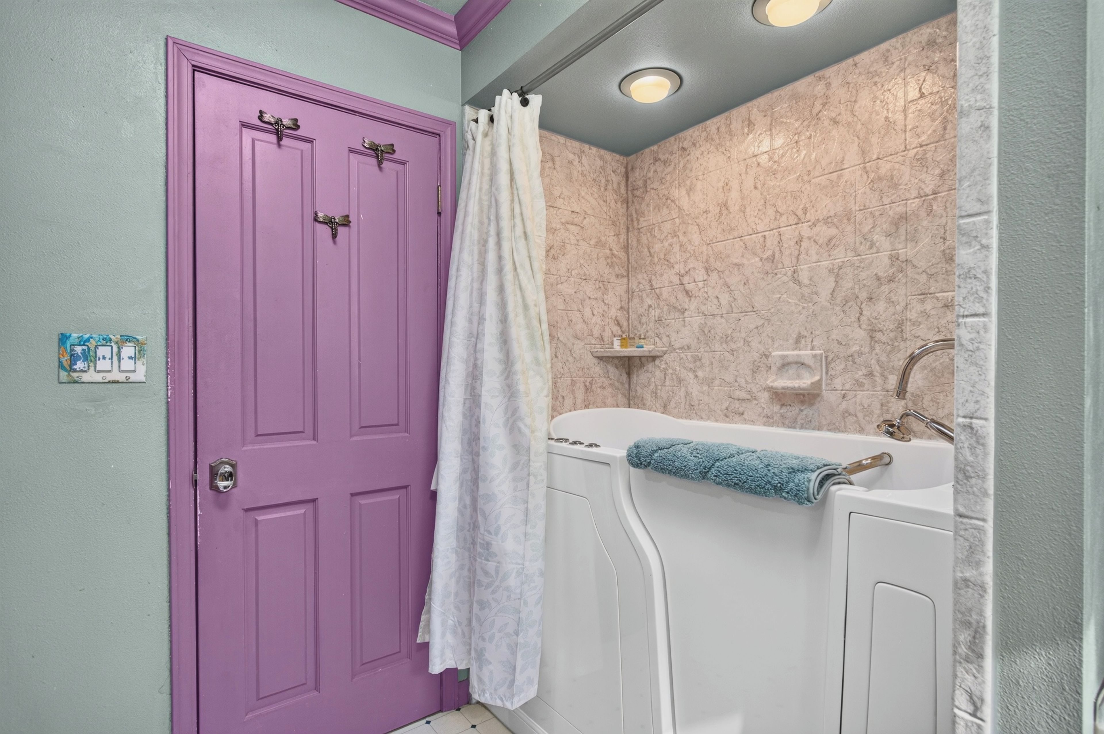 A bathroom with a purple door, a white bathtub, and a shower curtain.