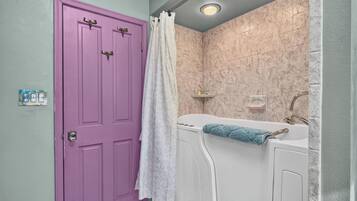 A bathroom with a purple door, a white bathtub, and a shower curtain.