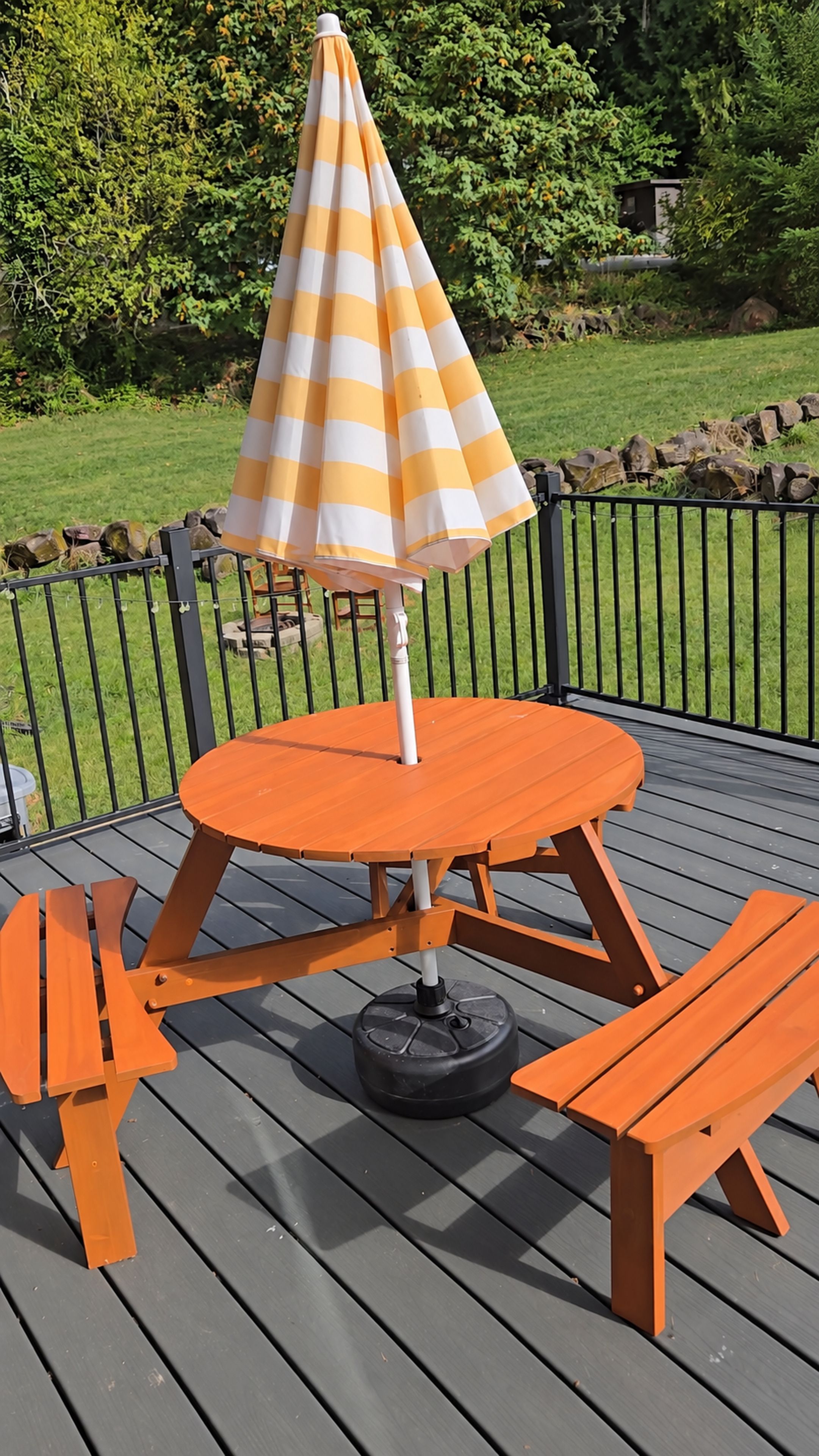 A wooden deck with a round table and benches, an umbrella, and a metal fence.