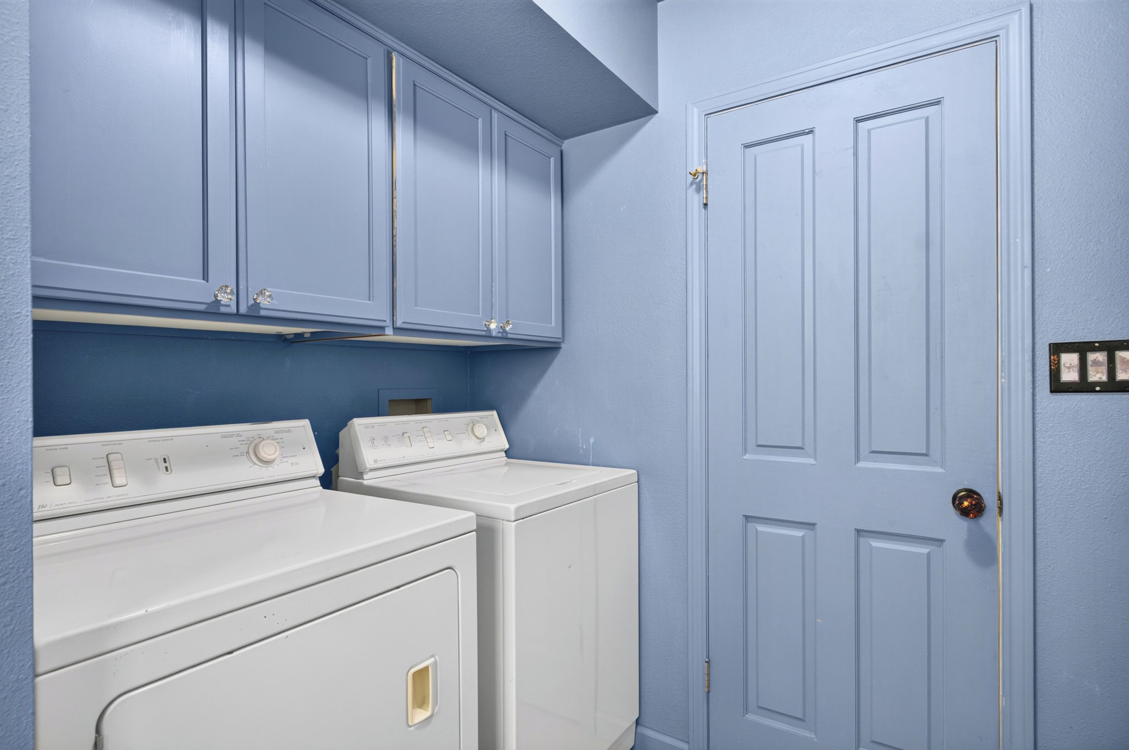 A laundry room with two white dryers and a blue door.