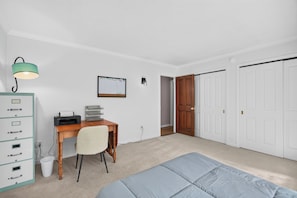 A bedroom with a desk, chair, bed, wardrobe, and a door leading to another room.