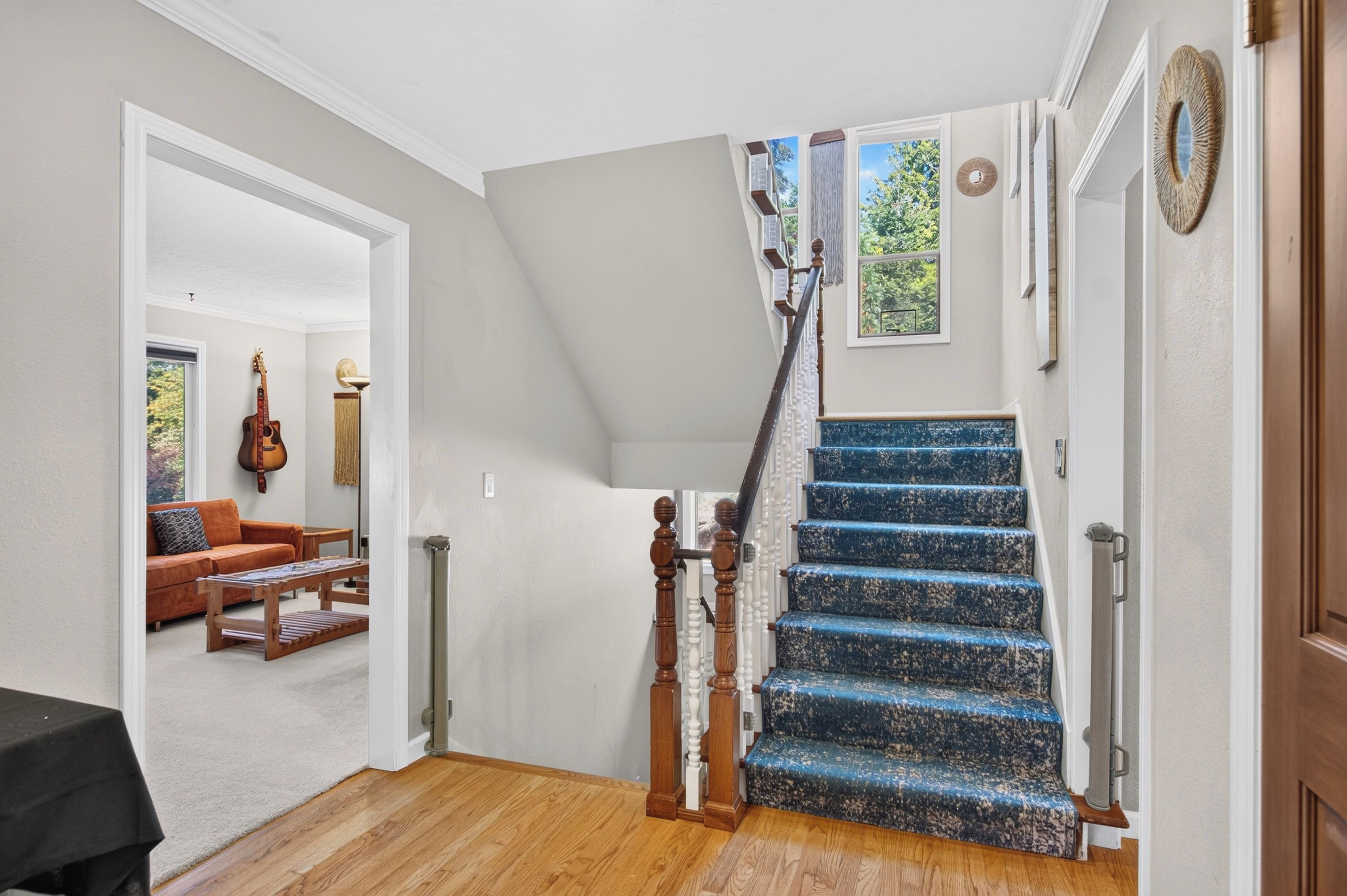 A staircase with blue steps leading to a landing, a wooden handrail, and a view of a living room with a sofa and a guitar.