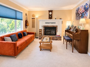 A living room with a fireplace, a sofa, a coffee table, a piano, and a clock on the wall.