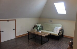 A room with a sloped ceiling, a single window, a sofa, a coffee table, and a door.