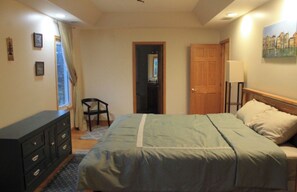 A bedroom with a bed, dresser, chair, and a door leading to another room.