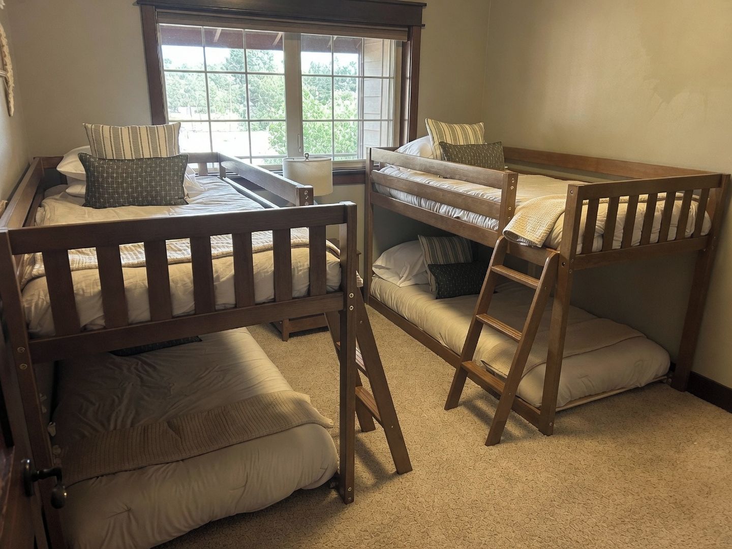A room with bunk beds, a window with a view of trees, and a door.