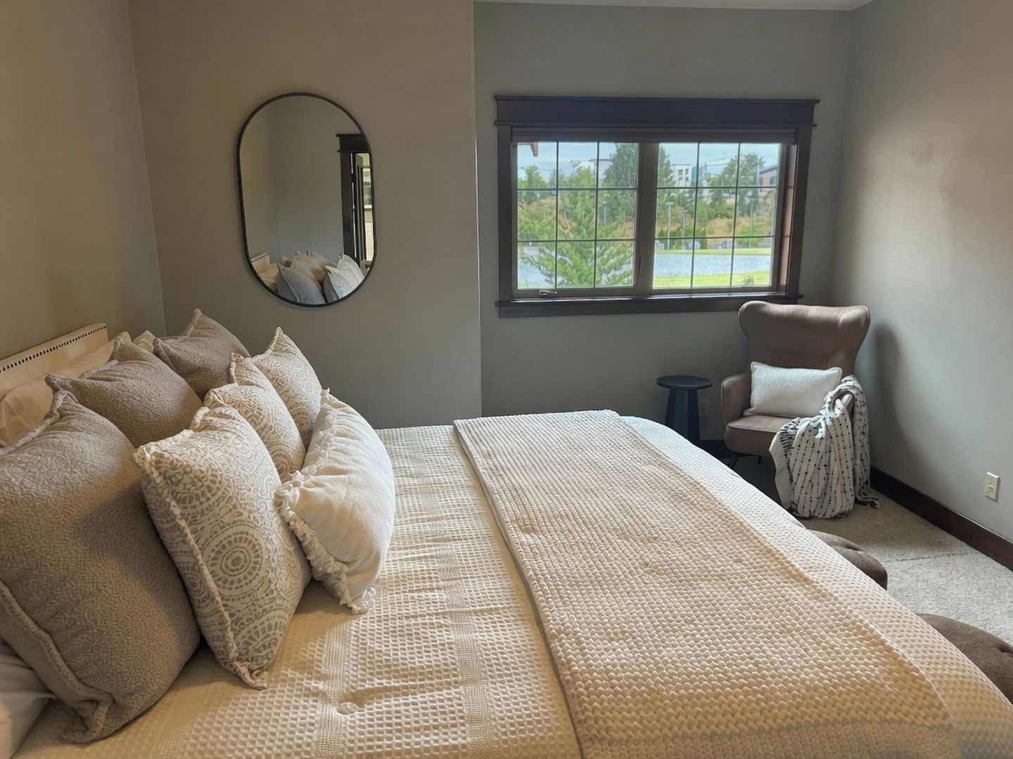 A bedroom with a large bed, a chair, a window with a view, and a mirror on the wall.