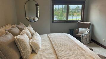 A bedroom with a large bed, a chair, a window with a view, and a mirror on the wall.