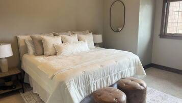 A bedroom with a large bed, two bedside lamps, a round mirror, and a window with blinds.