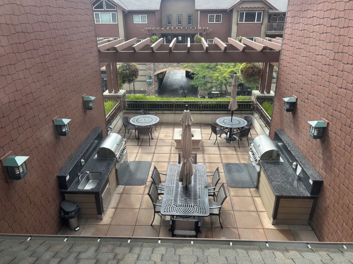 A covered outdoor patio with a grill, seating, and a view of a brick building.