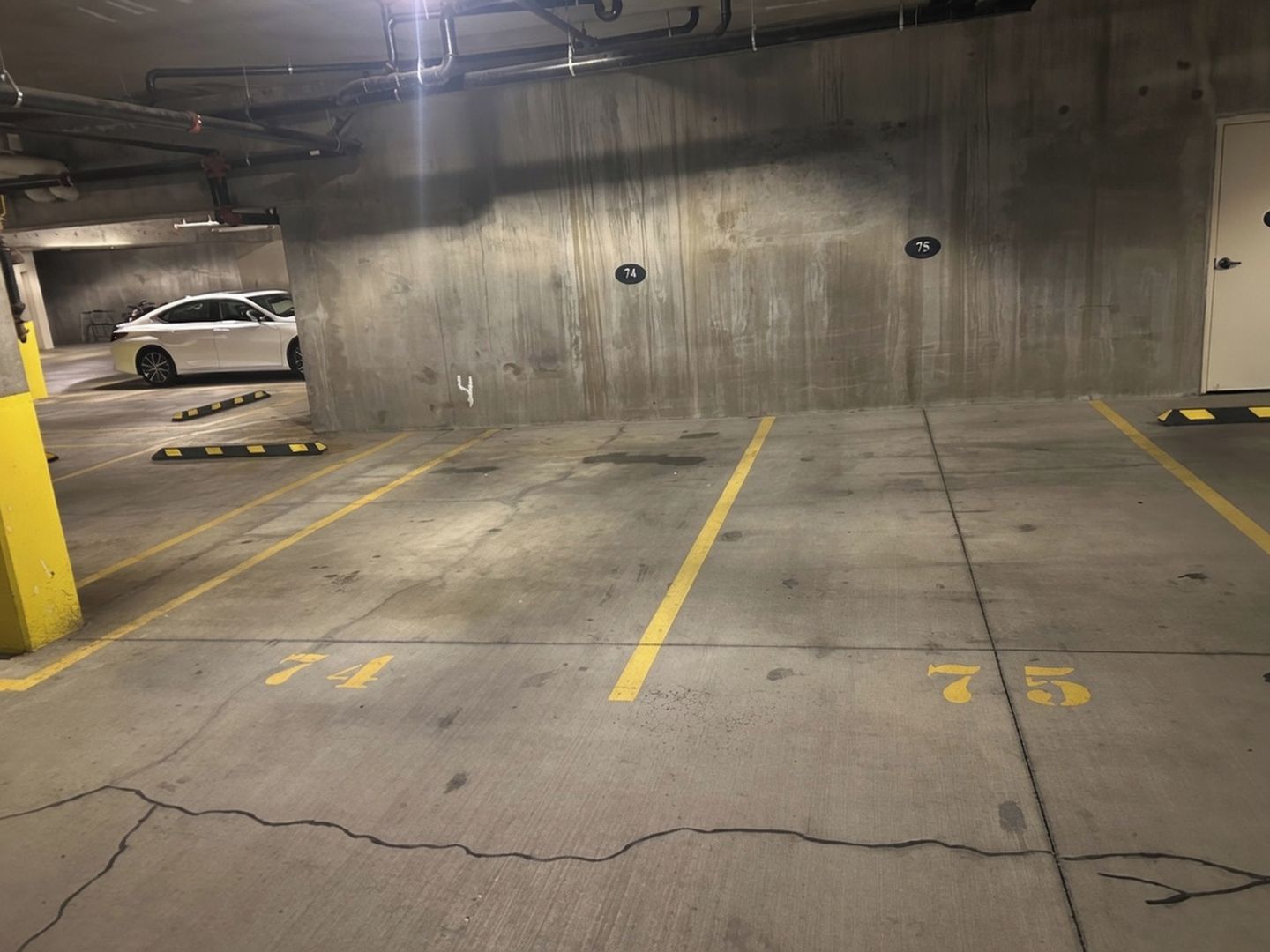 A parking garage with concrete walls, numbered parking spaces, and a white car parked in one of the spaces.