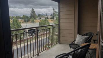 A balcony with two chairs and a table, overlooking a street with cars and trees.