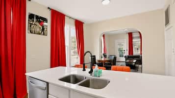 A modern kitchen with a white countertop, two sinks, and a dining area with a table and chairs.