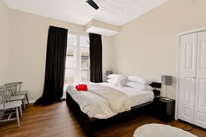 A bedroom with a bed, a desk, chairs, a wardrobe, and a window with curtains.