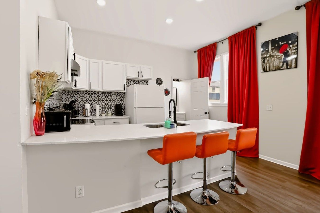 A modern kitchen with white cabinetry, a central island with bar stools, and a red curtain.