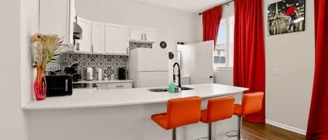 A modern kitchen with white cabinetry, a central island with bar stools, and a red curtain.