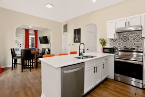 A modern kitchen with a central island, white cabinetry, stainless steel appliances, and a dining area with orange chairs. - Bright & Spacious Home Near Downtown Indy (Indianapolis)