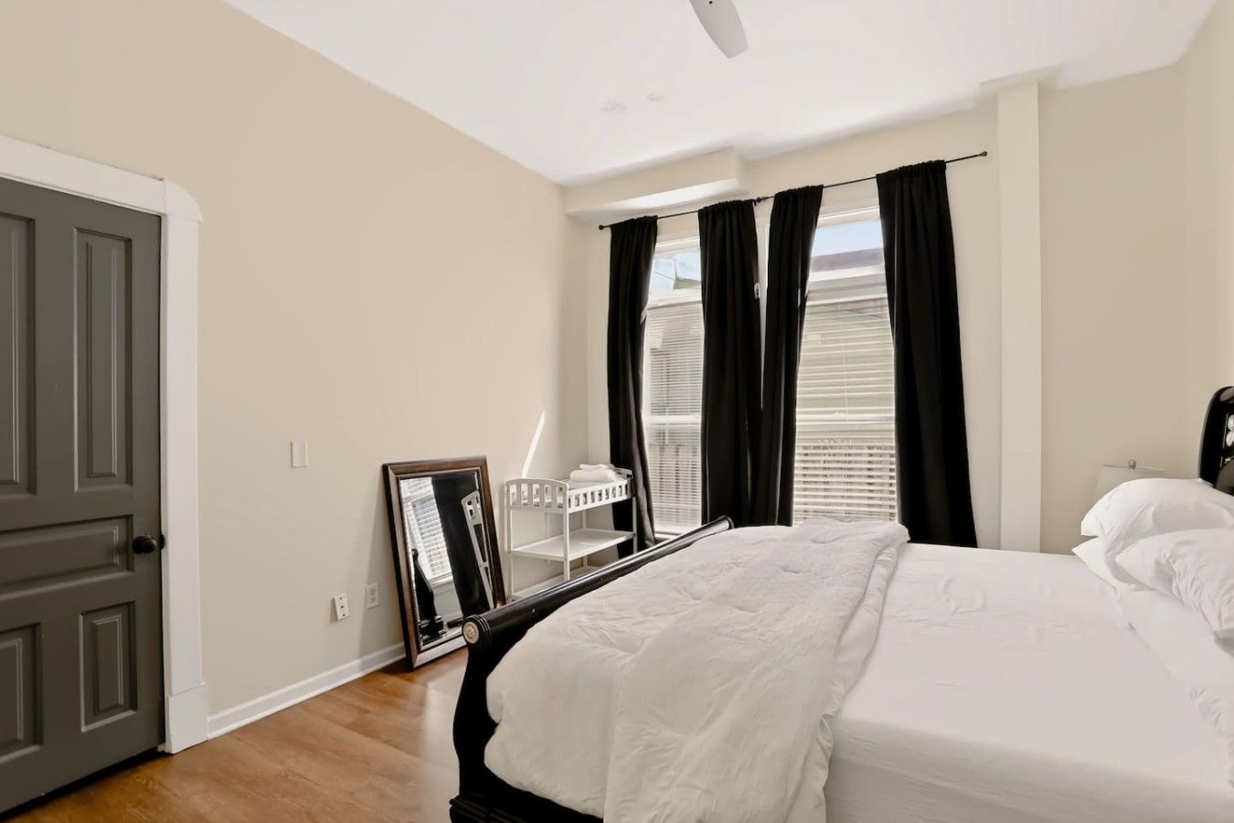 Un dormitorio con cama, espejo, ventana con cortinas y puerta.