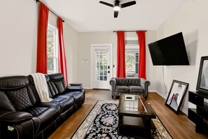 A living room with a black leather sofa, a grey sofa, a coffee table, a TV mounted on the wall, and a door with glass panels. - Bright & Spacious Home Near Downtown Indy (Indianapolis)