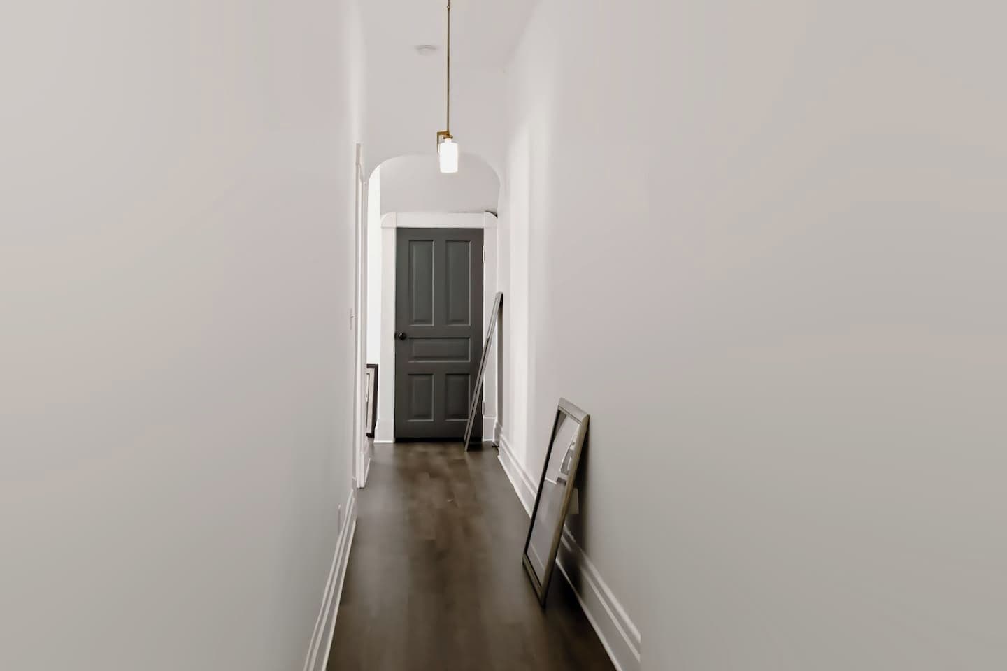 Un corridoio stretto con pavimento in legno scuro, pareti bianche e una porta in fondo.