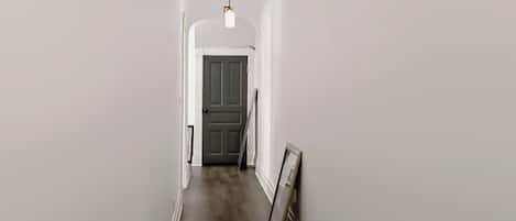 A narrow hallway with a dark wooden floor, white walls, and a door at the end.