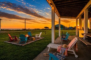 Eine Außenpatio-Terrasse mit Liegestühlen und einer Feuerstelle mit Blick auf ein Grasfeld und einen Sonnenuntergang.