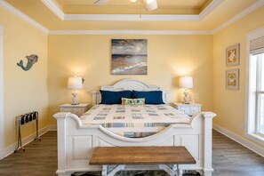 A bedroom with a large bed, two bedside tables, a bench, a painting, and a window. - Huge 5BR w/ Ocean View & Fire Pit (Port Bolivar)