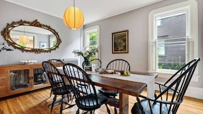 Une salle à manger avec une table en bois, des chaises noires, un miroir et une suspension.