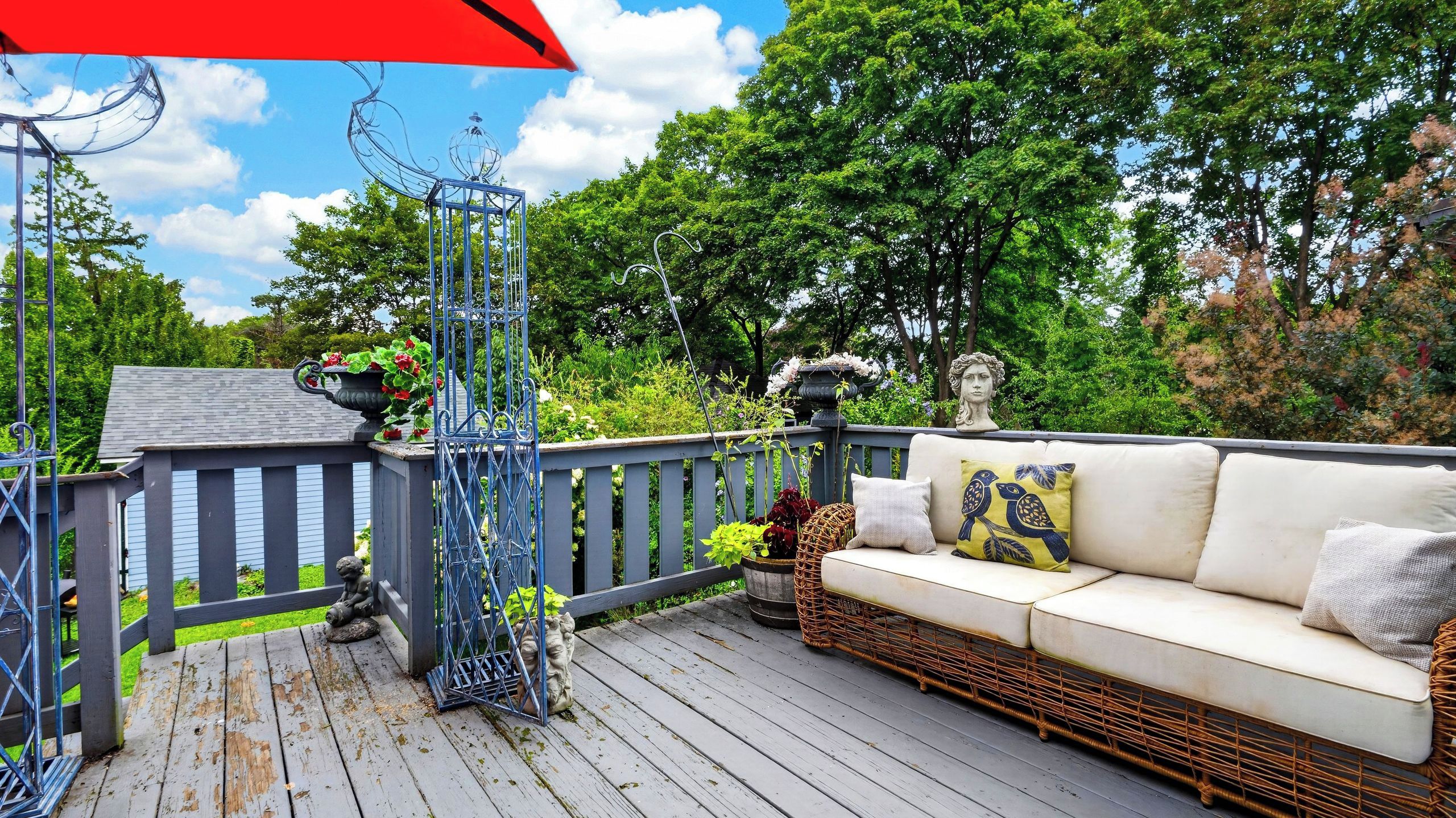 A wooden deck with a wicker sofa, a metal gate, and a statue of a child.