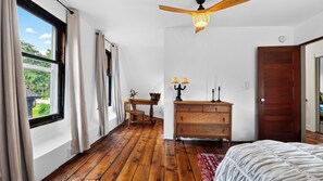 Ein Schlafzimmer mit Holzboden, einem Bett, einer Kommode, einem Schreibtisch mit Stuhl und einem Deckenventilator.