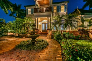 A two-story house with a front porch, a fountain, and a well-maintained garden. - Casa De La Cascada | Heated Pool with Grotto, Outdoor Kitchen, Steps to Hillview District (Sarasota)