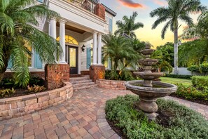 A house with a brick entrance, a fountain, and a well-maintained garden. - Casa De La Cascada | Heated Pool with Grotto, Outdoor Kitchen, Steps to Hillview District (Sarasota)
