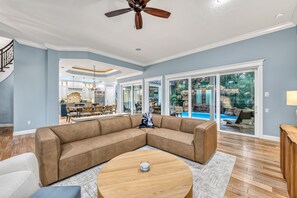 A spacious living room with a large sectional sofa, a round coffee table, and a ceiling fan. - Casa De La Cascada | Heated Pool with Grotto, Outdoor Kitchen, Steps to Hillview District (Sarasota)