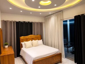 A modern bedroom with a wooden bed, a bedside table with a plant, and a view of the outside through a window.
