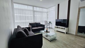 A modern living room with a sofa, coffee table, TV, and a fireplace.