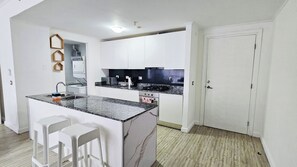 A modern kitchen with white cabinets, a granite countertop, a built-in oven, and a small island with bar stools.