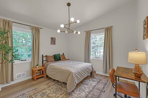 Ein Schlafzimmer mit einem Bett, Nachttischen, einem Schreibtisch, einem Stuhl, einer Lampe und einer Pendelleuchte.