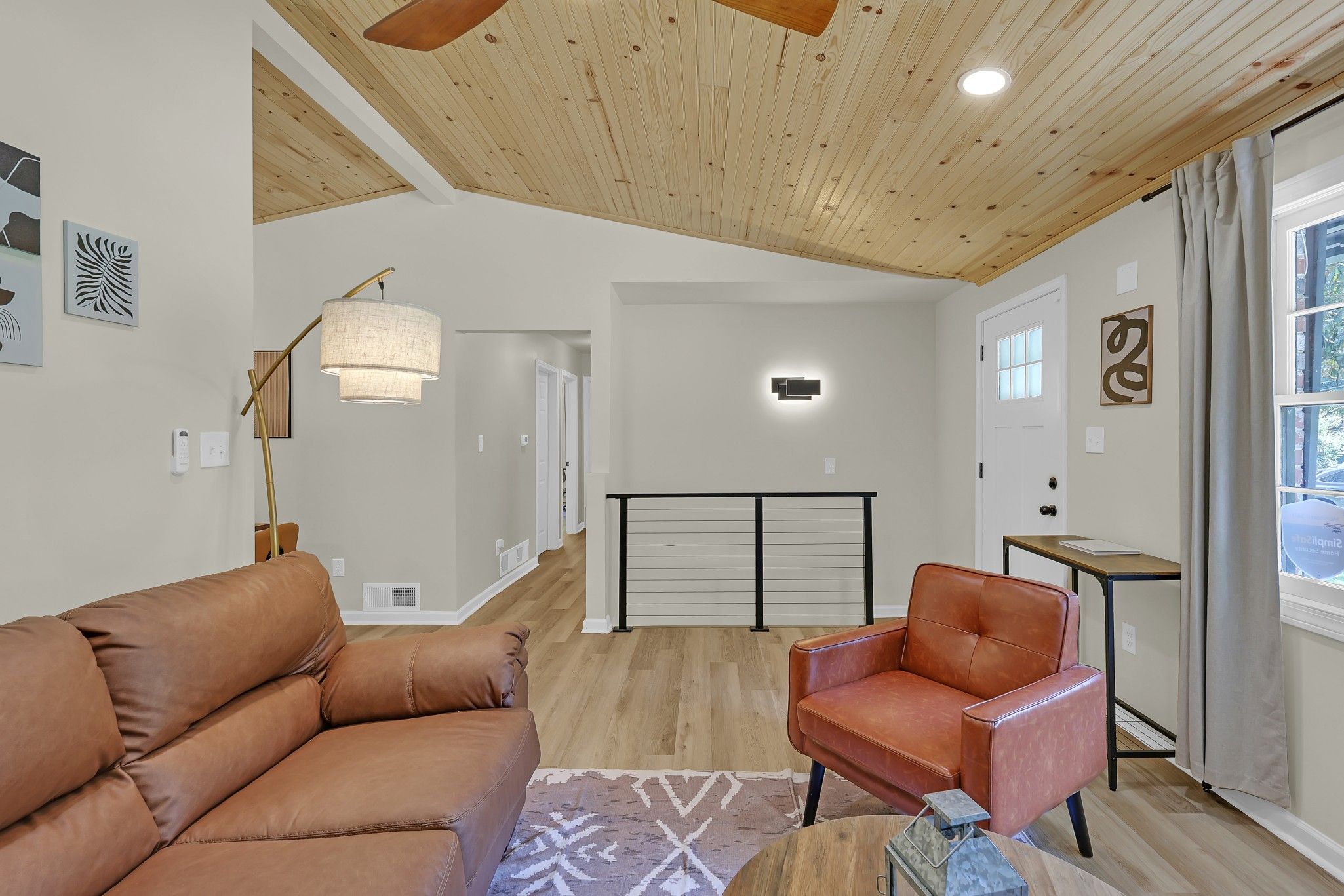 Una sala de estar moderna con un sofá de cuero marrón, un sillón de cuero rojo, una lámpara de pie y un tapete estampado.