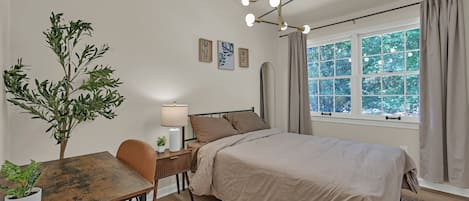Une chambre à coucher avec un lit, une table de chevet, une lampe, une plante en pot et une fenêtre avec des rideaux.