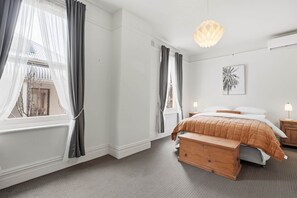 A bedroom with a bed, a nightstand, a lamp, a wooden bench, and a wall-mounted light fixture. - Ethelea Retreat – 2 Bedroom – Walk to Restaurant Precinct (North Hobart)