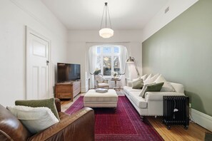 A living room with a television, a sofa, a coffee table, and a radiator. - Ethelea Retreat – 2 Bedroom – Walk to Restaurant Precinct (North Hobart)