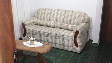 Ett vardagsrum med en randig soffa, ett litet bord med en vas och ett grönt, kaklat golv.