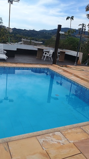Une piscine dont le bord est revêtu de carrelage, entourée d’un patio aménagé avec une table et des chaises.